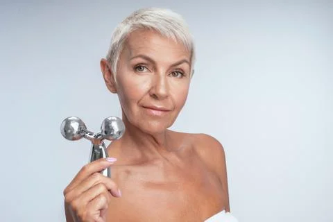 A pretty middle aged woman holding a metal face roller to the camera Stock Photos