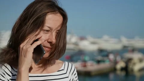 A pretty middle-aged woman is talking on the phone on the street on a sunny Видео 157449906