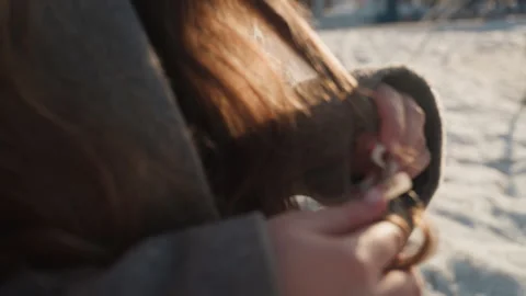 Pretty model adjusting pendant on snowy shore, gray coat and flowing hair in Stock Footage 342431341