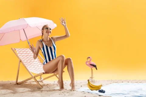 Pretty model in beach clothes poses waving hand and smiling Фото