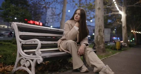 Pretty model in classical coat posing sitting on the bench at night city Video stock 319669811