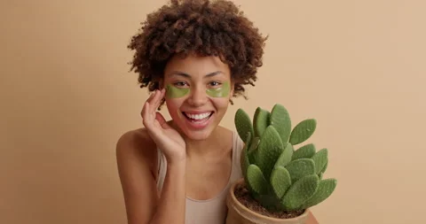 Pretty positive dark skinned young woman with Afro hair applies beauty patches Stock Footage 145348420