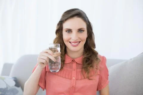 Pretty pregnant woman showing glass of water sitting on couch Stock Photos