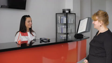 Pretty senior lady checking in at the doctor's office reception desk Stock Footage 61468443