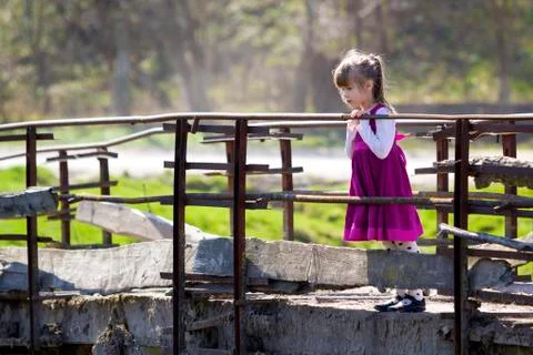 Pretty small blond long haired girl in nice red dress stands alone on old cem Stock-Fotos