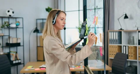 Pretty smiling experienced successful blond woman in headphones holding laptop Stock Footage 158008116