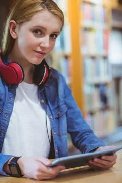 Pretty student with headphones using tablet in library Stockfoto's
