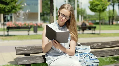 Pretty student reading book on the bench and smiling to the camera Stock-Footage 67369260