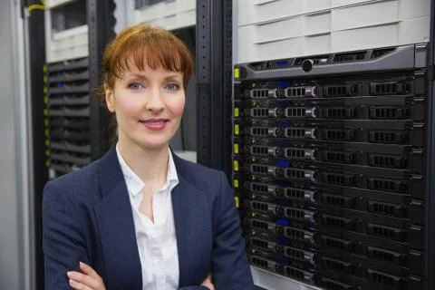 Pretty technician smiling at camera beside server tower Stock Photos