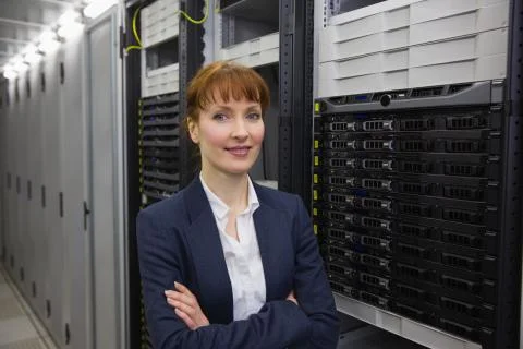 Pretty technician smiling at camera beside server tower Stock Photos