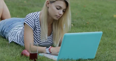 Pretty woman blogger working with her laptop outdoor sitting on grass in park Stock Footage