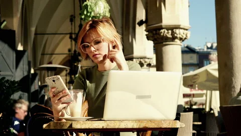 Pretty woman comparing data on smartphone and laptop in cafe in the city, 4K Stock Footage 140275710