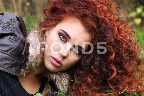 Pretty woman with curly hair in jacket on grass in field, shallow dof Stock Photos