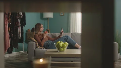 Pretty woman eats a red apple, lying on sofa and and speaks via video link Stock Footage 151923764