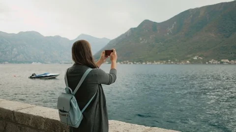 Pretty Woman in gray cardigan photographs mountains on the phone near the sea Stock Footage