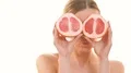 The pretty woman holding two halves of a grapefruit on the white background 4k or 4k+ Resolution