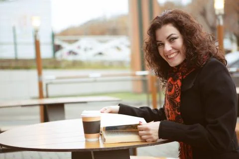 A pretty woman laughs merrily while reading a fascinating book on the terrace of Stock Photos