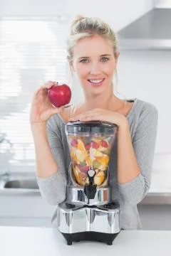 Pretty woman leaning on her juicer full of fruit and holding red apple Stock Photos