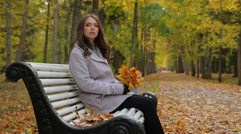 Pretty woman  with maple leaves sitting on a bench in a beautiful autumn park. Stock Footage 55674152