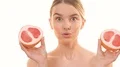 The pretty woman posing with two halves of a grapefruit on the white background 4k or 4k+ Resolution