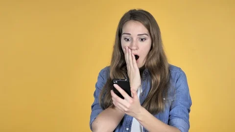 Pretty Woman in Shock while Using Smartphone Isolated on Yellow Background Stock Footage 99013599