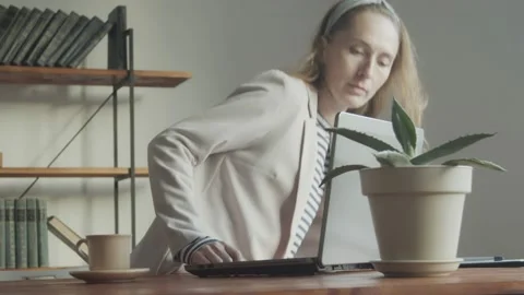 A pretty woman sits down at the table and starts working on a laptop. Freelancer Stock Footage 233008498