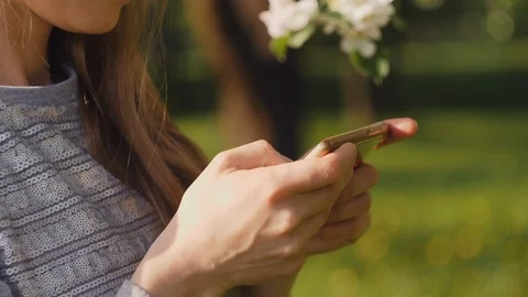 Pretty woman sms texting using smartphone on background of a blooming branch of Stock Footage 120043419
