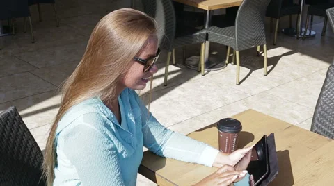 Pretty woman use a tablet computer drink coffee sitting in a cafe in the summer Stock Footage 68816014