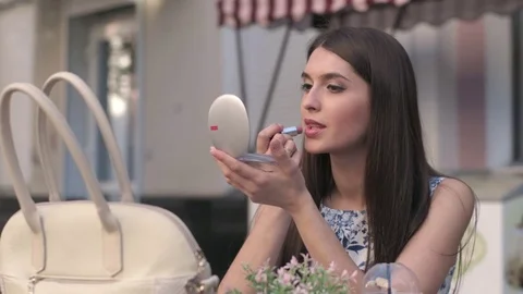 Pretty, woman using lipgloss while painting her lips in the outdoor cafe Vidéo 78912207