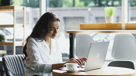 Pretty worker in white shirt typing on computer with smile and drinking from Stock Footage 117119665