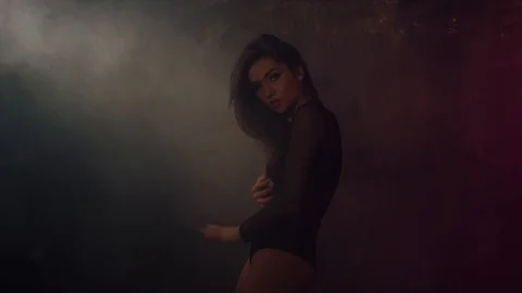 Pretty young brunette is dancing alone in a dark hall, moving her slim body 스톡 동영상 99561525
