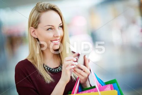 Pretty young customer with cellphone spending leisure in shopping center Stock Photos