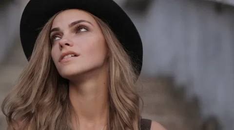 Pretty young girl in a black hat looking up on a gray background Video stock 67284053