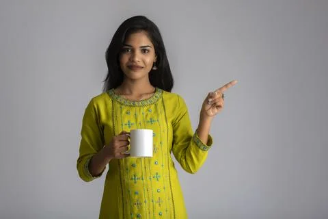 Pretty young girl with a cup of tea or coffee posing on grey background Stock Photos