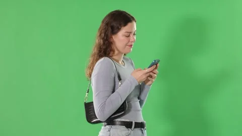 Pretty young girl scrolling through smartphone screen against a green screen Stock Footage 341785176