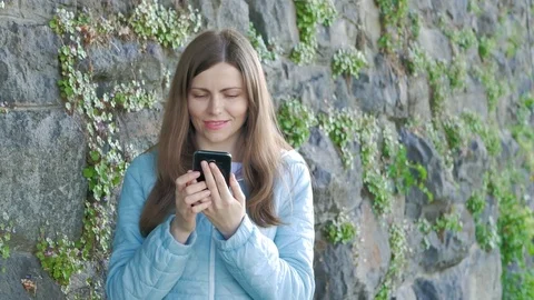 Pretty young girl using smartphone. Vintage wall of wild stone in the background Stock Footage 82522998
