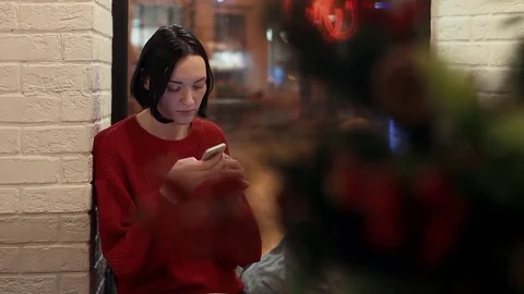 Pretty young girl using smartphone in cafe in evening. Christmas time Stock Footage 83082983