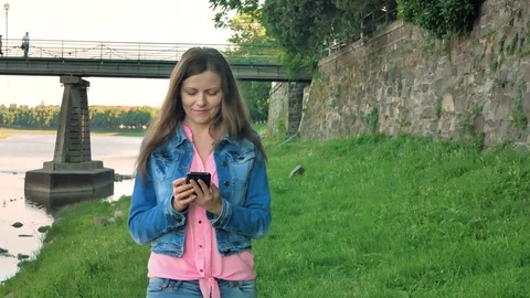 Pretty young girl walks along the waterfront using smartphone. Bridge and Stock Footage
