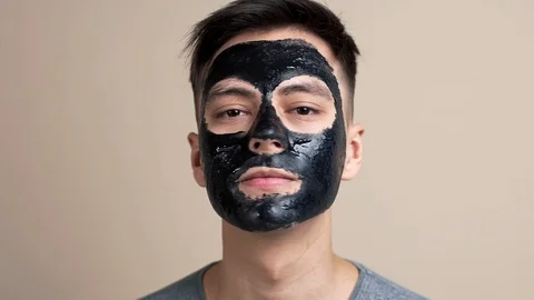 Pretty young guy in black cosmetic face mask looks to the camera in slow motion Stock Footage 101376644