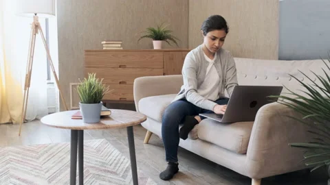 Pretty young lady sitting on couch at home, using laptop, watching videos Stock Footage 158236872