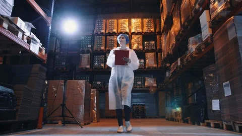 Pretty young lady walking between shelves in huge storage room and making notes Stock Footage 98031667