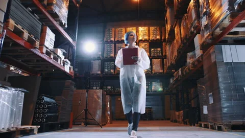 Pretty young lady walking between shelves in huge storage room and making notes Stock Footage 152449890
