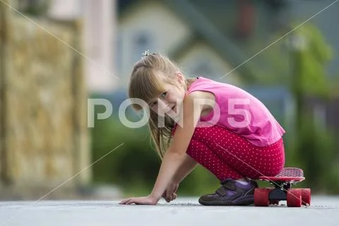 Pretty young long-haired blond child girl in casual pink clothing sits leanin Stock Photos