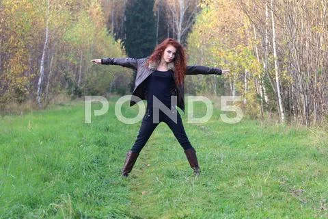 Pretty young woman in leather jacket poses on grass in autumn forest Stock Photos