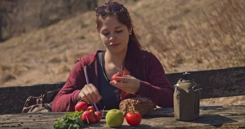Pretty young woman is resting while hiking and preparing radishes at a table Stock Footage 105407445