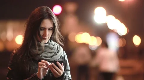 Pretty young woman smiling, using her smartphone at night. Lady in the street in Stock Footage 67950415