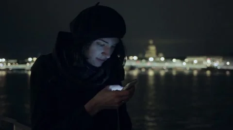 Pretty young woman smiling, using her smartphone. Night city cold weather cold Stock Footage 69058166