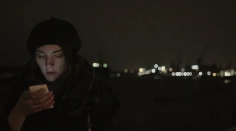 Pretty young woman smiling, using her smartphone. Night city cold weather warm Video stock 69060313