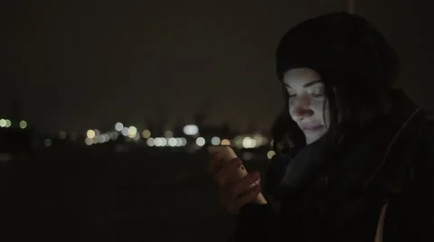 Pretty young woman smiling, using her smartphone. Night city cold weather warm Stock Footage 69060506