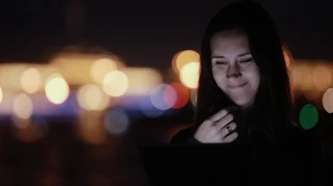 Pretty young woman using tablet, smiling at night. Blurred coloured city lights Stock Footage 67950063